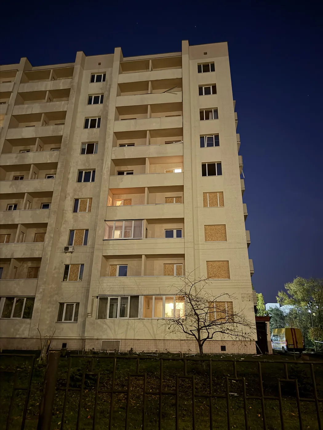 The State Transport University dormitory at night, its broken windows boarded up with OSB panels, October 2026