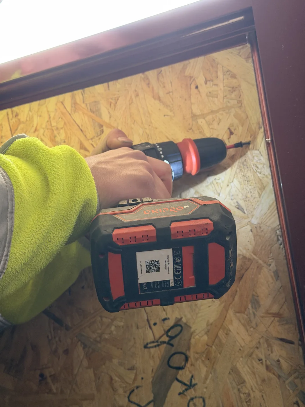 A GURTUM drill with its Shelf QR label fixing an OSB panel into a window frame at the dormitory, October 2026