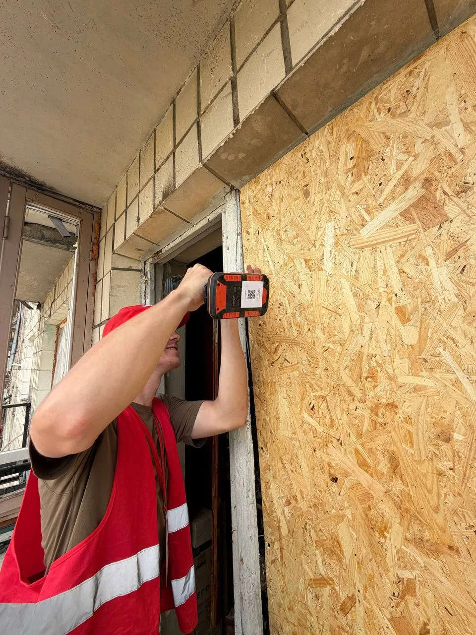 A GURTUM volunteer boards up a window frame with a drill carrying its Shelf QR label, July 2026