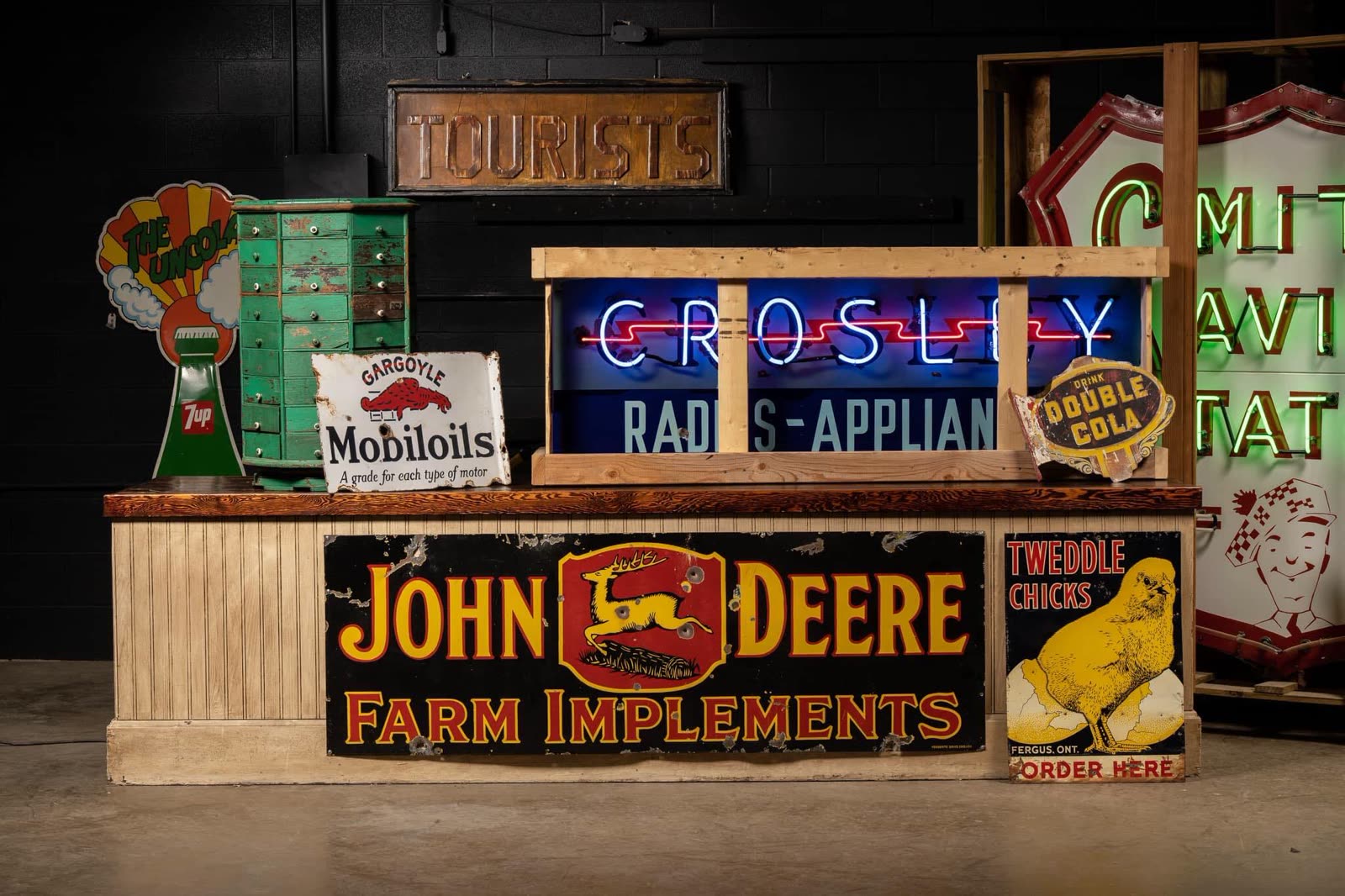 Auction lots staged at Rock Auction Gallery — enamel signs, a Crosley neon, a John Deere Farm Implements sign