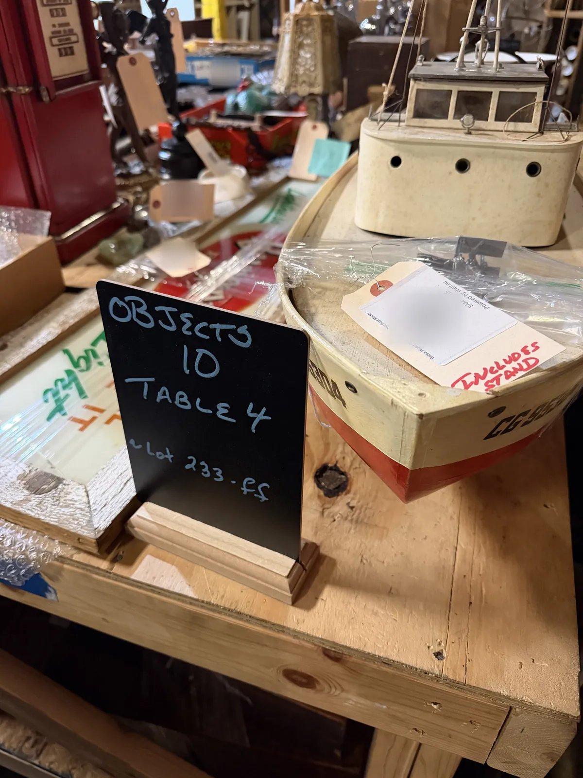 Chalkboard sign reading "Objects 10, Table 4, Lot 233 ff" next to a model boat carrying its Shelf label